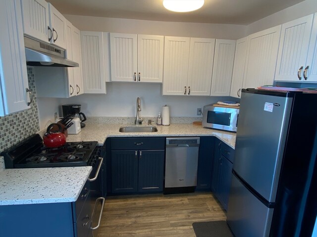 kitchen with light hardwood / wood-style floors, sink, backsplash, white cabinetry, and appliances with stainless steel finishes