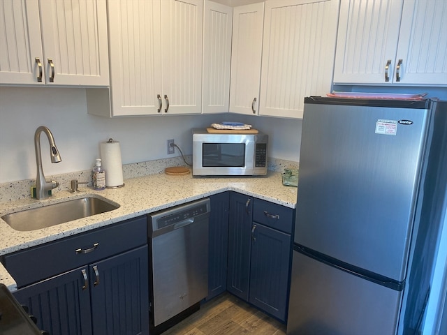 kitchen featuring stainless steel appliances, light stone counters, white cabinets, hardwood / wood-style flooring, and sink