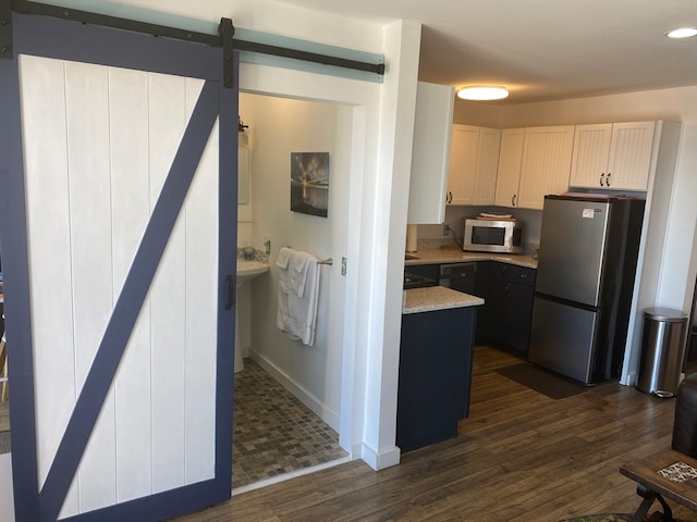 kitchen featuring dark hardwood / wood-style flooring, white cabinetry, a barn door, and stainless steel appliances