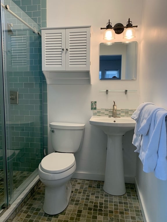 bathroom featuring a shower with door and toilet