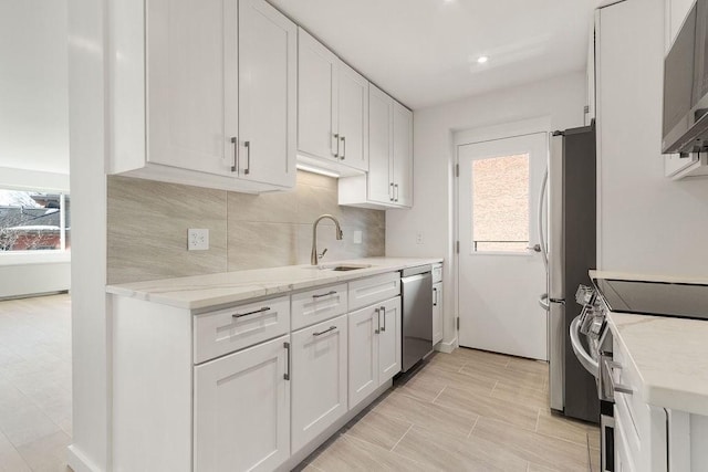 kitchen featuring sink, appliances with stainless steel finishes, white cabinetry, tasteful backsplash, and light stone countertops