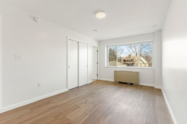 unfurnished bedroom featuring radiator, light wood-type flooring, and a closet