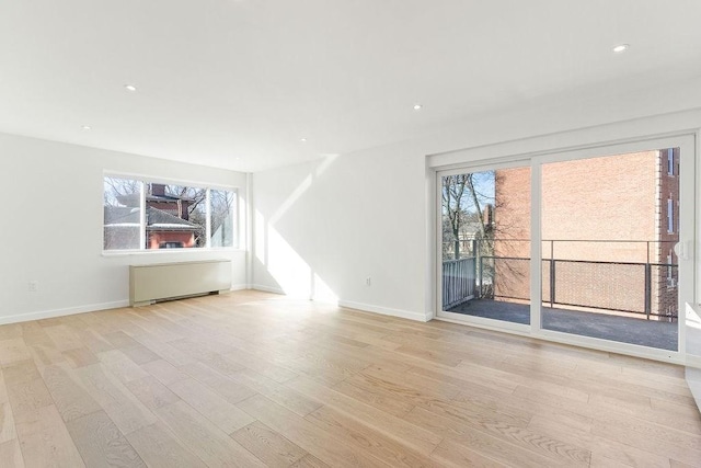 unfurnished living room with radiator, light hardwood / wood-style floors, and a healthy amount of sunlight