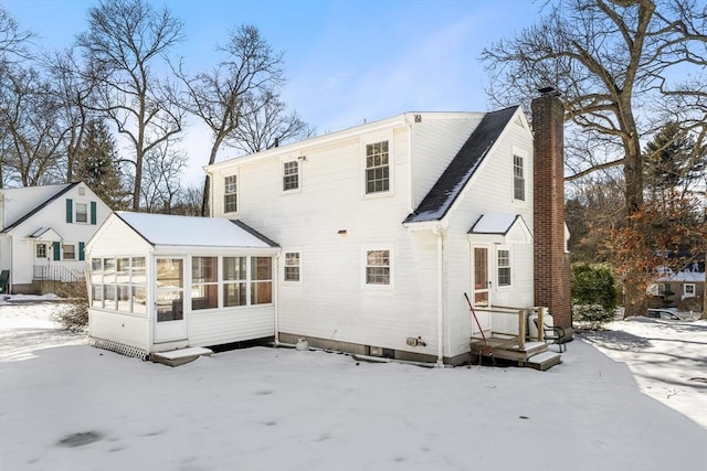 snow covered back of property with a sunroom