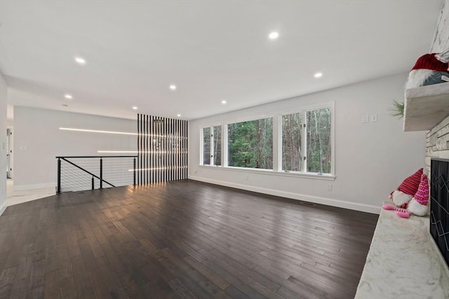 unfurnished living room featuring a stone fireplace and dark hardwood / wood-style flooring