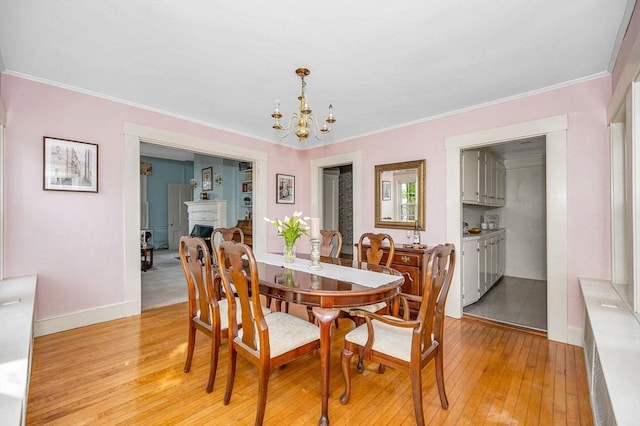 dining room with a notable chandelier, a fireplace, crown molding, and light wood-style floors