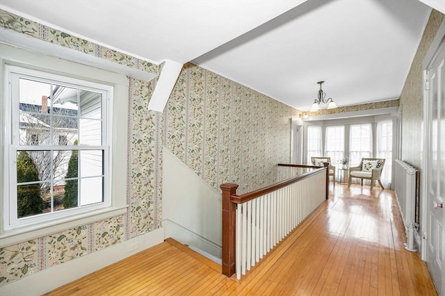 corridor featuring radiator, wallpapered walls, a notable chandelier, an upstairs landing, and light wood-type flooring