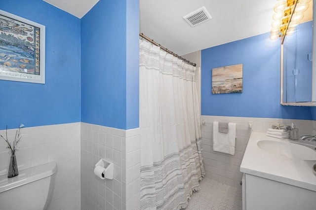 bathroom featuring vanity, a wainscoted wall, visible vents, tile walls, and toilet