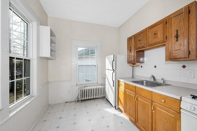 kitchen with radiator, wainscoting, brown cabinets, white appliances, and a sink