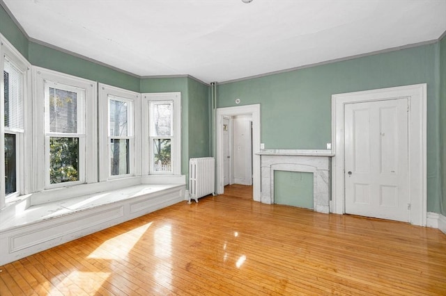 unfurnished living room with radiator, a fireplace, light wood-type flooring, and crown molding