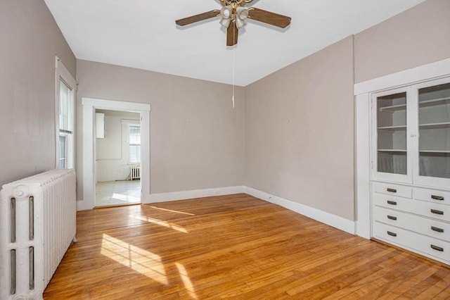 unfurnished room with light wood finished floors, ceiling fan, radiator, and baseboards