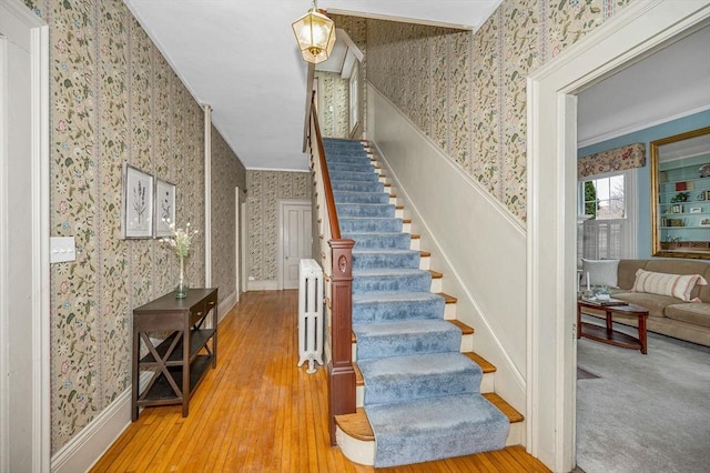 stairway featuring baseboards, wood finished floors, ornamental molding, and wallpapered walls