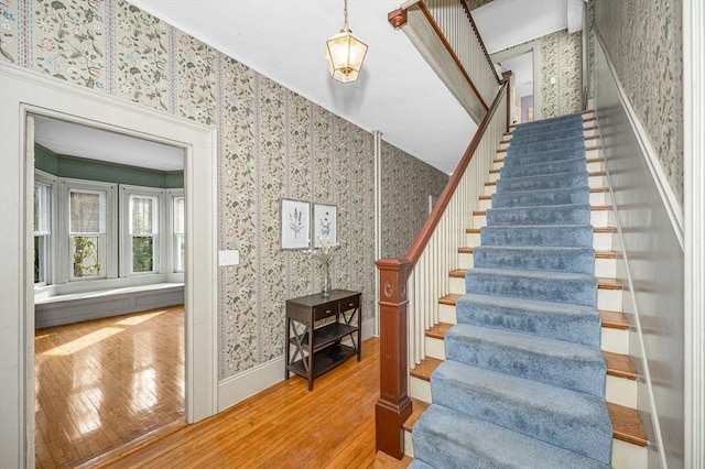 stairway with wallpapered walls, baseboards, and hardwood / wood-style floors