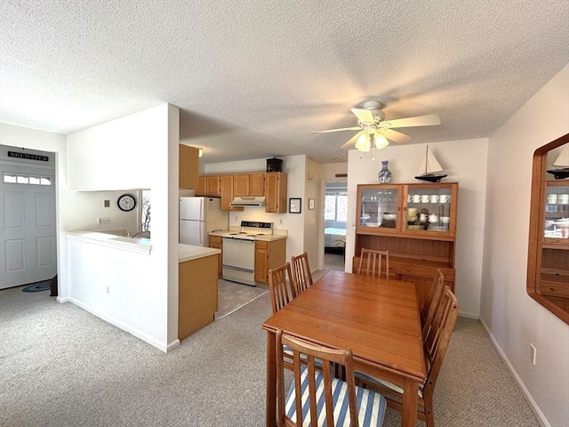 dining room with a textured ceiling, a ceiling fan, light colored carpet, and baseboards