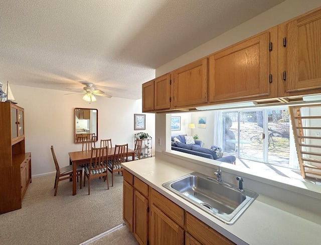 kitchen with ceiling fan, light countertops, light carpet, a textured ceiling, and a sink