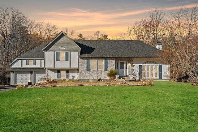 tri-level home with roof with shingles, driveway, an attached garage, a yard, and a chimney