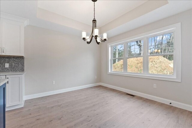 unfurnished dining area with an inviting chandelier, light wood-type flooring, and a tray ceiling