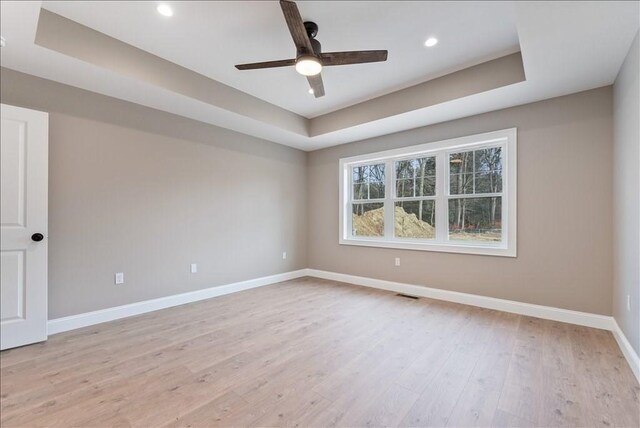 unfurnished room featuring ceiling fan, light wood-type flooring, and a tray ceiling