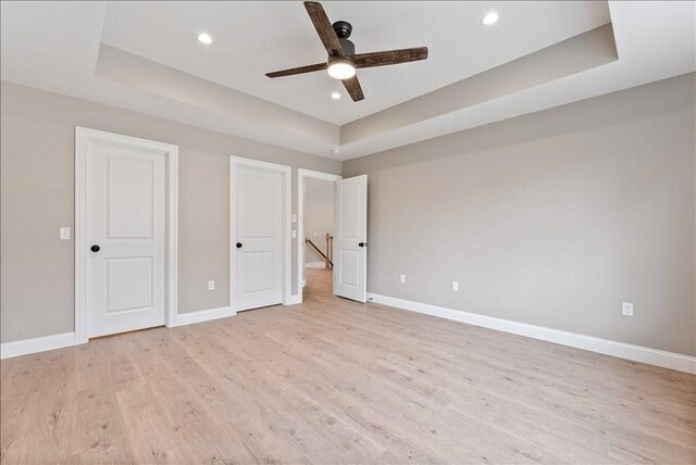 unfurnished bedroom with light hardwood / wood-style flooring, a raised ceiling, and ceiling fan