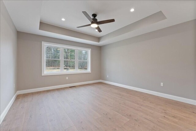 unfurnished room with a raised ceiling, ceiling fan, and light wood-type flooring