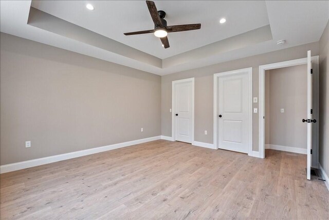 unfurnished bedroom with light hardwood / wood-style flooring, ceiling fan, and a tray ceiling