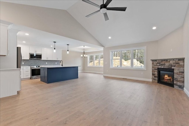 unfurnished living room featuring sink, high vaulted ceiling, light wood-type flooring, a fireplace, and ceiling fan with notable chandelier