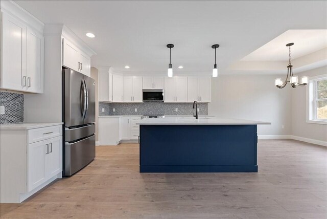 kitchen with pendant lighting, appliances with stainless steel finishes, a kitchen island with sink, light hardwood / wood-style floors, and white cabinets