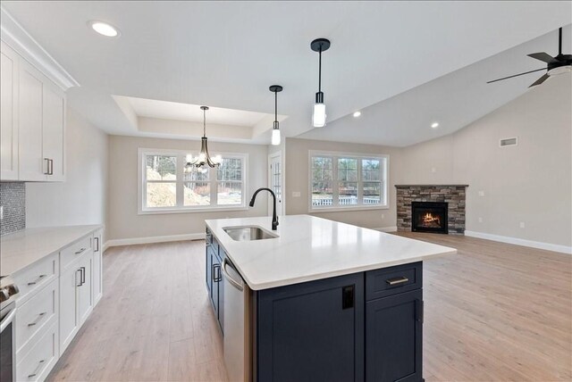 kitchen featuring sink, appliances with stainless steel finishes, a tray ceiling, a kitchen island with sink, and white cabinets