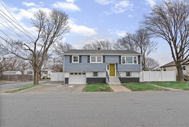 bi-level home featuring an attached garage, driveway, a chimney, and fence