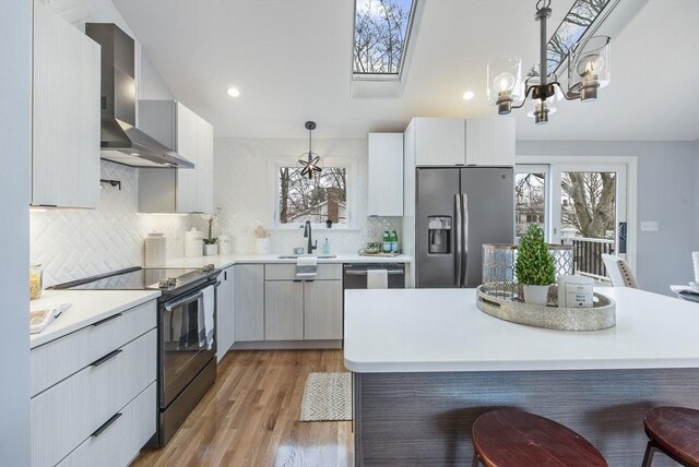 kitchen with stainless steel fridge with ice dispenser, a healthy amount of sunlight, wall chimney exhaust hood, black electric range, and a sink