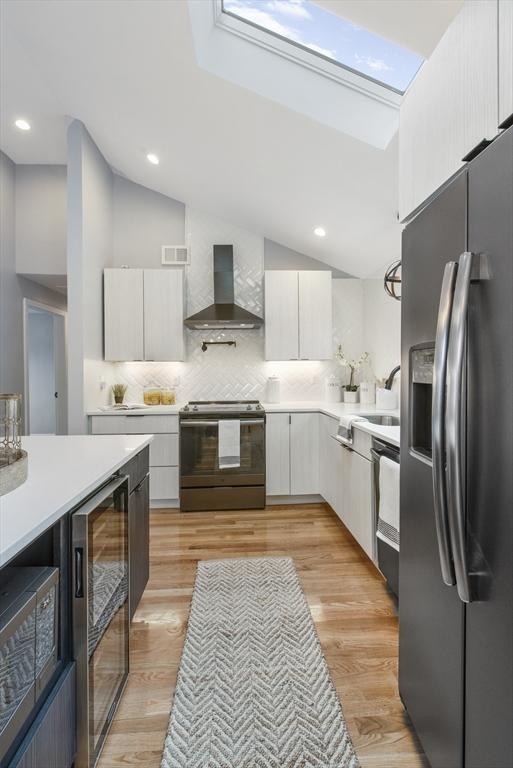 kitchen featuring wall chimney exhaust hood, wine cooler, light countertops, stainless steel refrigerator with ice dispenser, and range with electric stovetop