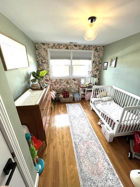 bedroom with an accent wall, wood finished floors, and wallpapered walls