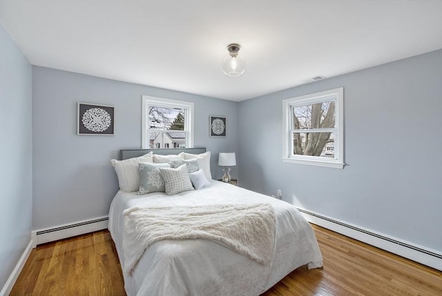 bedroom featuring multiple windows, baseboard heating, and wood finished floors