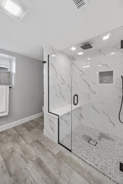 full bath with toilet, a marble finish shower, visible vents, and baseboards