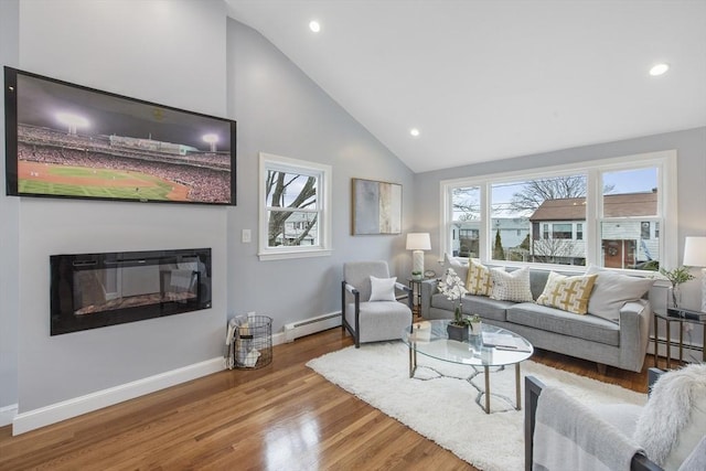 living area with high vaulted ceiling, wood finished floors, baseboards, baseboard heating, and a glass covered fireplace