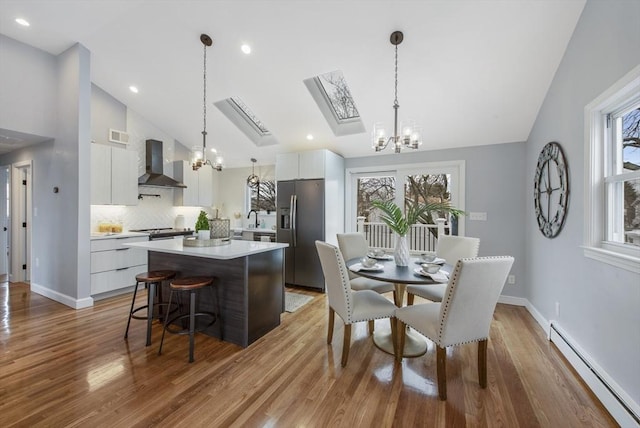 dining space with light wood finished floors, a skylight, baseboards, baseboard heating, and a chandelier