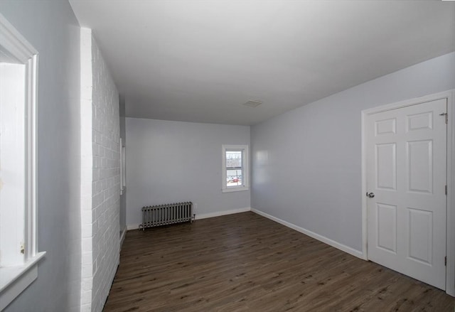 spare room with baseboards, radiator heating unit, and dark wood-type flooring