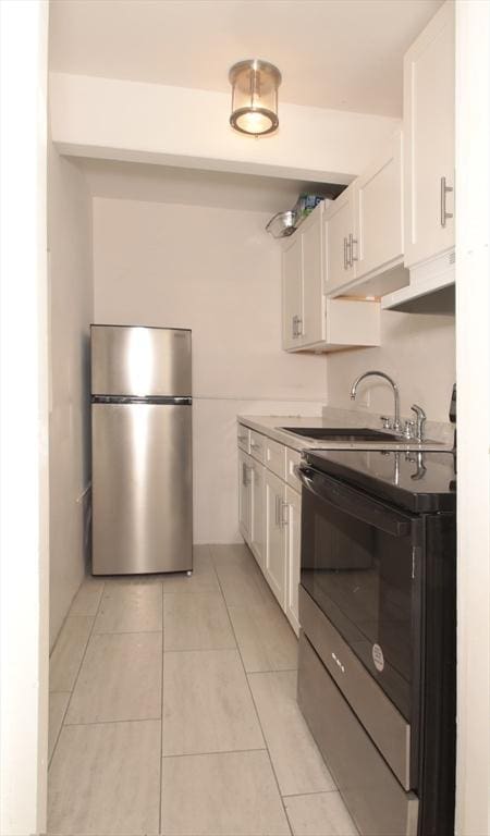 kitchen featuring range with electric cooktop, a sink, white cabinetry, freestanding refrigerator, and light tile patterned flooring