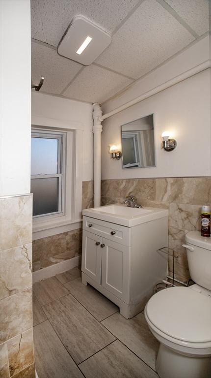 half bath with vanity, tile walls, toilet, and a paneled ceiling