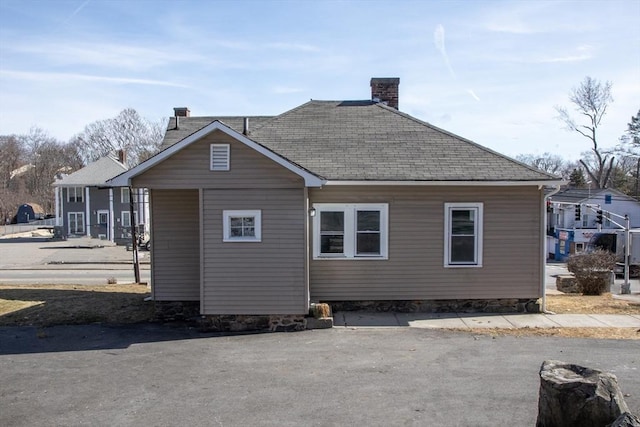 rear view of property featuring a chimney and roof with shingles