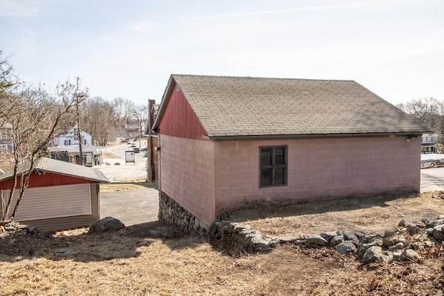 view of home's exterior featuring concrete block siding, an outdoor structure, and a shingled roof