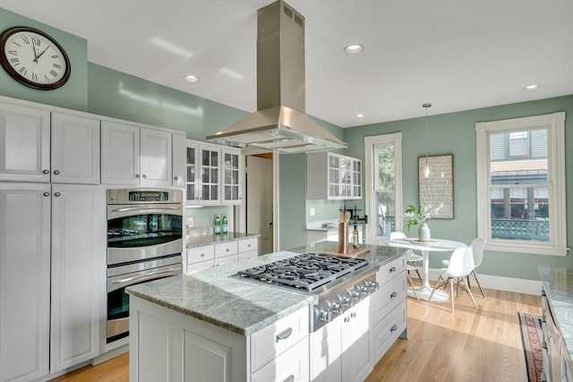 kitchen with appliances with stainless steel finishes, island exhaust hood, white cabinetry, and pendant lighting