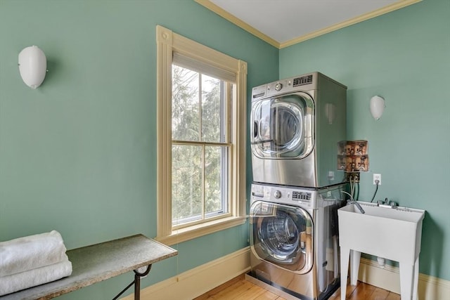 laundry room featuring stacked washing maching and dryer, ornamental molding, hardwood / wood-style flooring, and sink