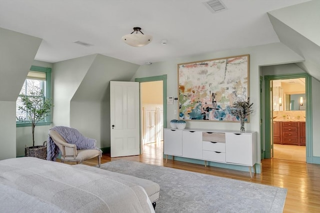 bedroom with ensuite bathroom, lofted ceiling, and light hardwood / wood-style floors