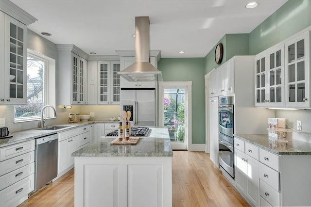 kitchen featuring light stone countertops, appliances with stainless steel finishes, a center island, sink, and island range hood