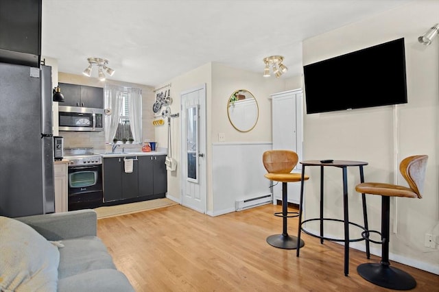 kitchen featuring a baseboard heating unit, stainless steel appliances, tasteful backsplash, sink, and light wood-type flooring