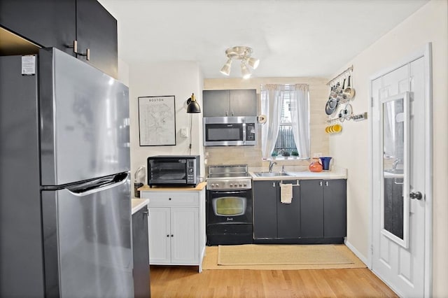 kitchen with sink, light wood-type flooring, white cabinetry, decorative backsplash, and stainless steel appliances