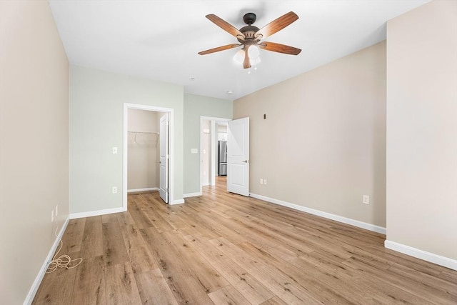 unfurnished bedroom with light wood-style flooring, freestanding refrigerator, a spacious closet, baseboards, and a closet