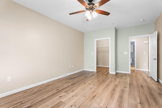 unfurnished bedroom with light wood finished floors, a closet, a walk in closet, baseboards, and ceiling fan