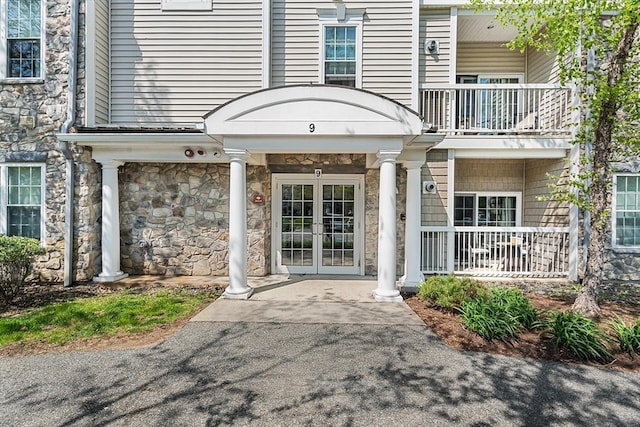 property entrance featuring a balcony, stone siding, and french doors